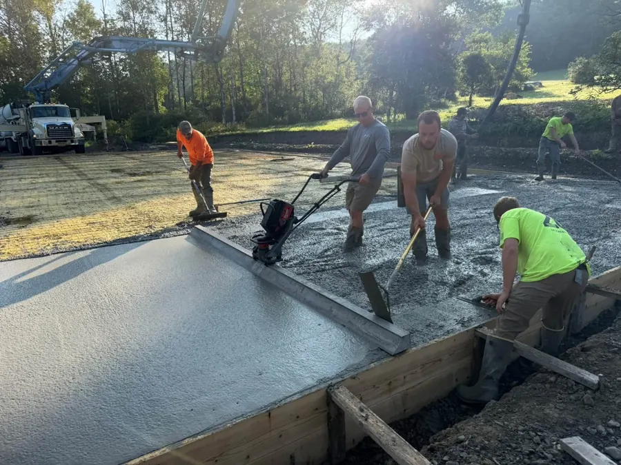 Crew running a power screed and raking concrete on a large slab pour
