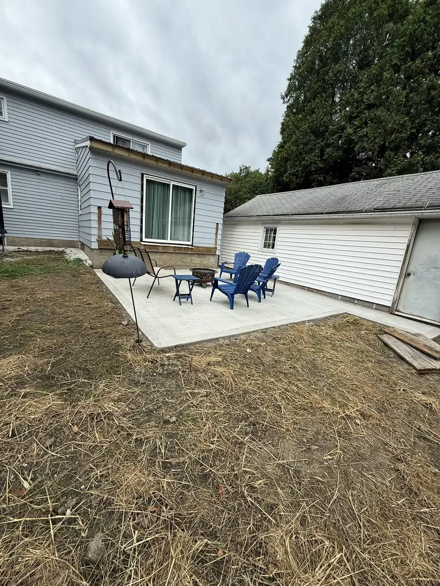 New concrete patio with blue chairs behind a house and garage