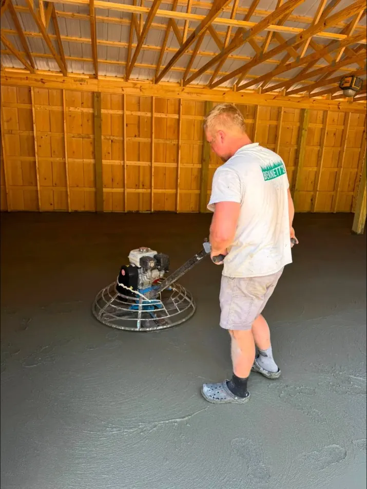 Power troweling a new concrete floor inside a pole building
