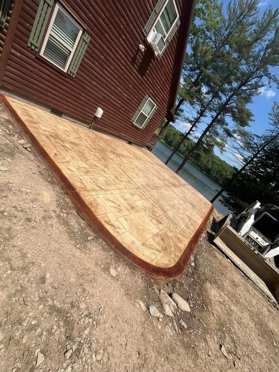 Tan stamped concrete patio with a curved edge beside a red house