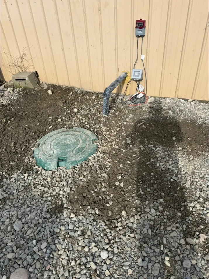 Finished stone backfill around a tank riser beside a commercial building