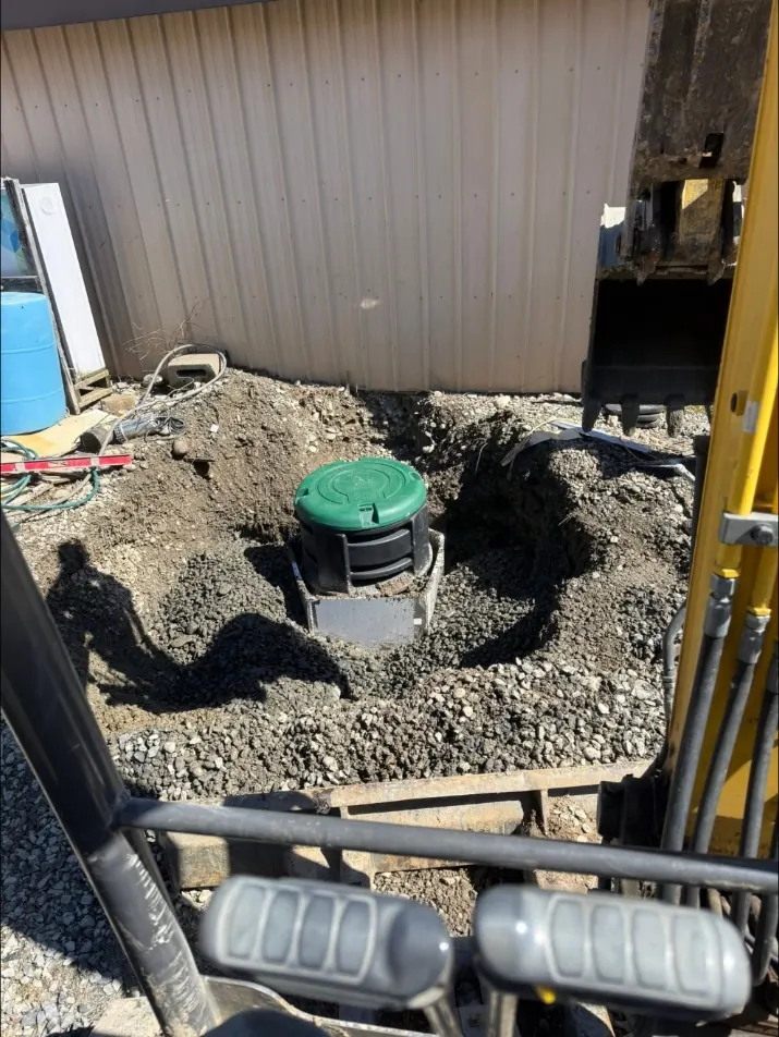 Mini excavator setting a tank and riser beside a commercial building