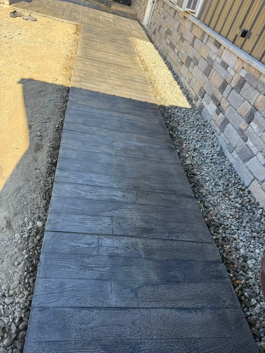 Gray wood plank stamped concrete walkway along a stone wall